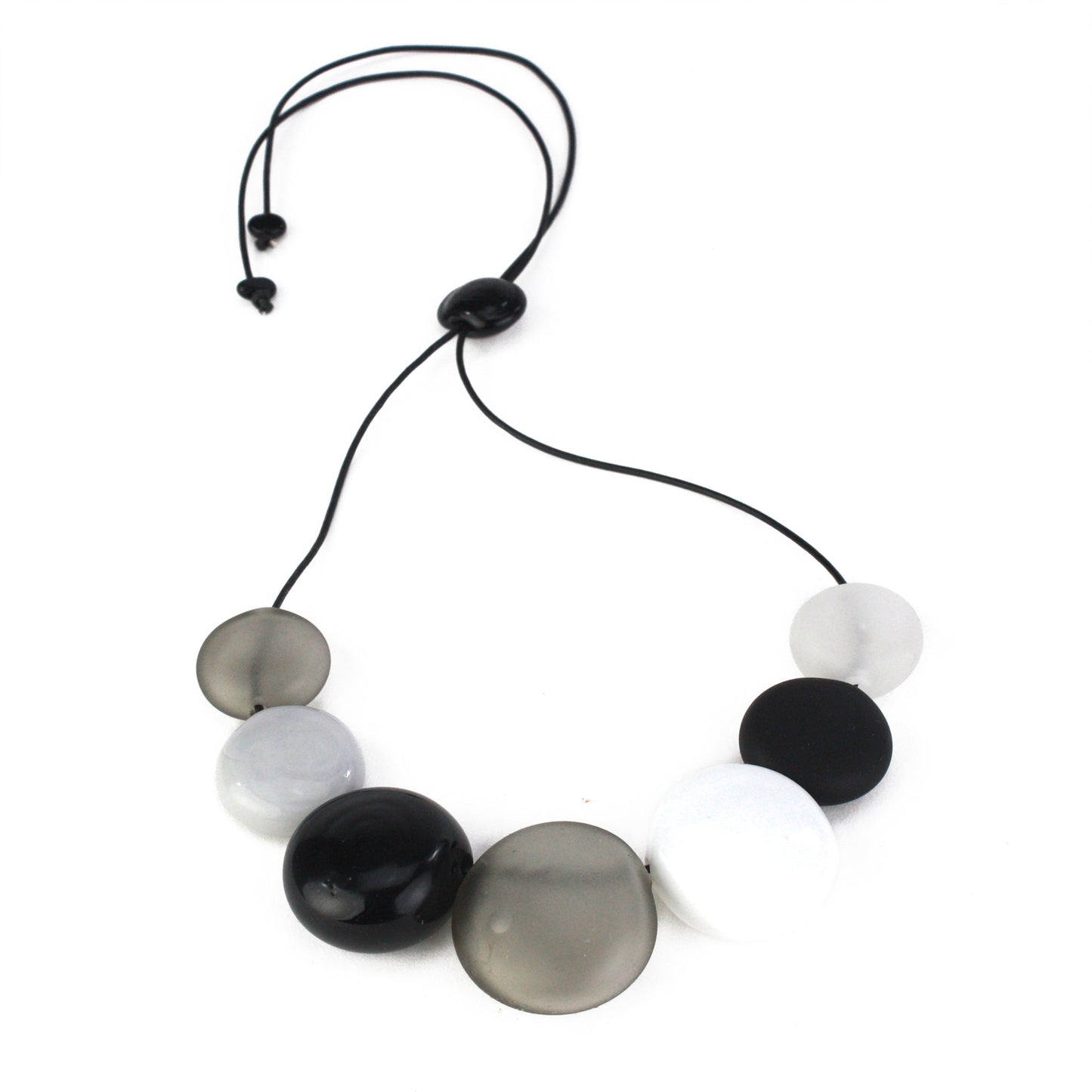 A monochromatic necklace featuring seven hollow, hand-blown glass beads in black, white, grey, and clear tones, strung on adjustable leather for versatile styling.