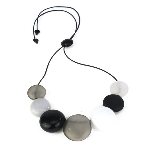 A monochromatic necklace featuring seven hollow, hand-blown glass beads in black, white, grey, and clear tones, strung on adjustable leather for versatile styling.