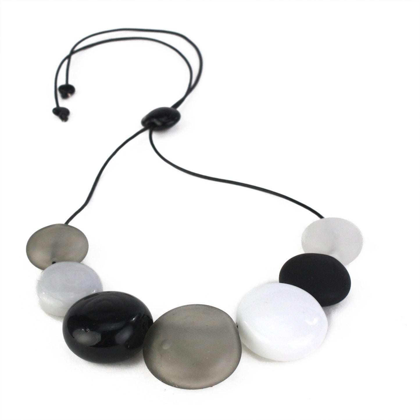 A monochromatic necklace featuring seven hollow, hand-blown glass beads in black, white, grey, and clear tones, strung on adjustable leather for versatile styling.