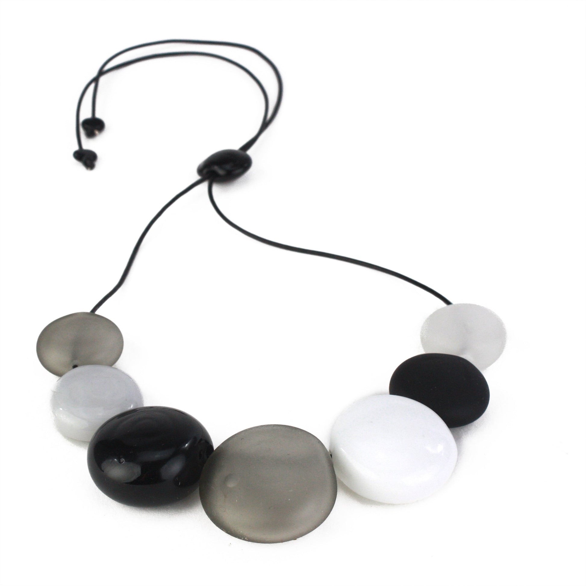 A monochromatic necklace featuring seven hollow, hand-blown glass beads in black, white, grey, and clear tones, strung on adjustable leather for versatile styling.