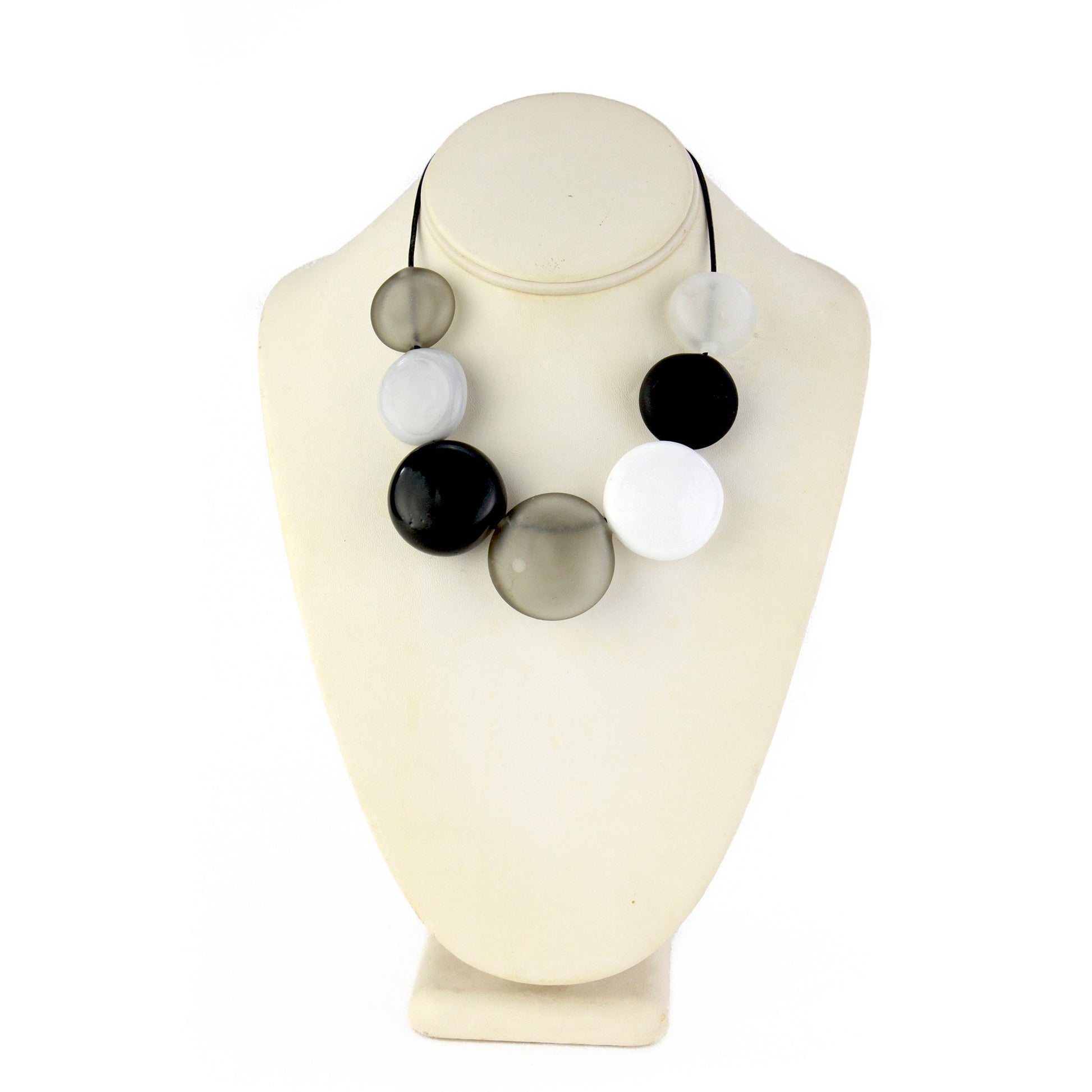 A monochromatic necklace featuring seven hollow, hand-blown glass beads in black, white, grey, and clear tones, strung on adjustable leather for versatile styling.