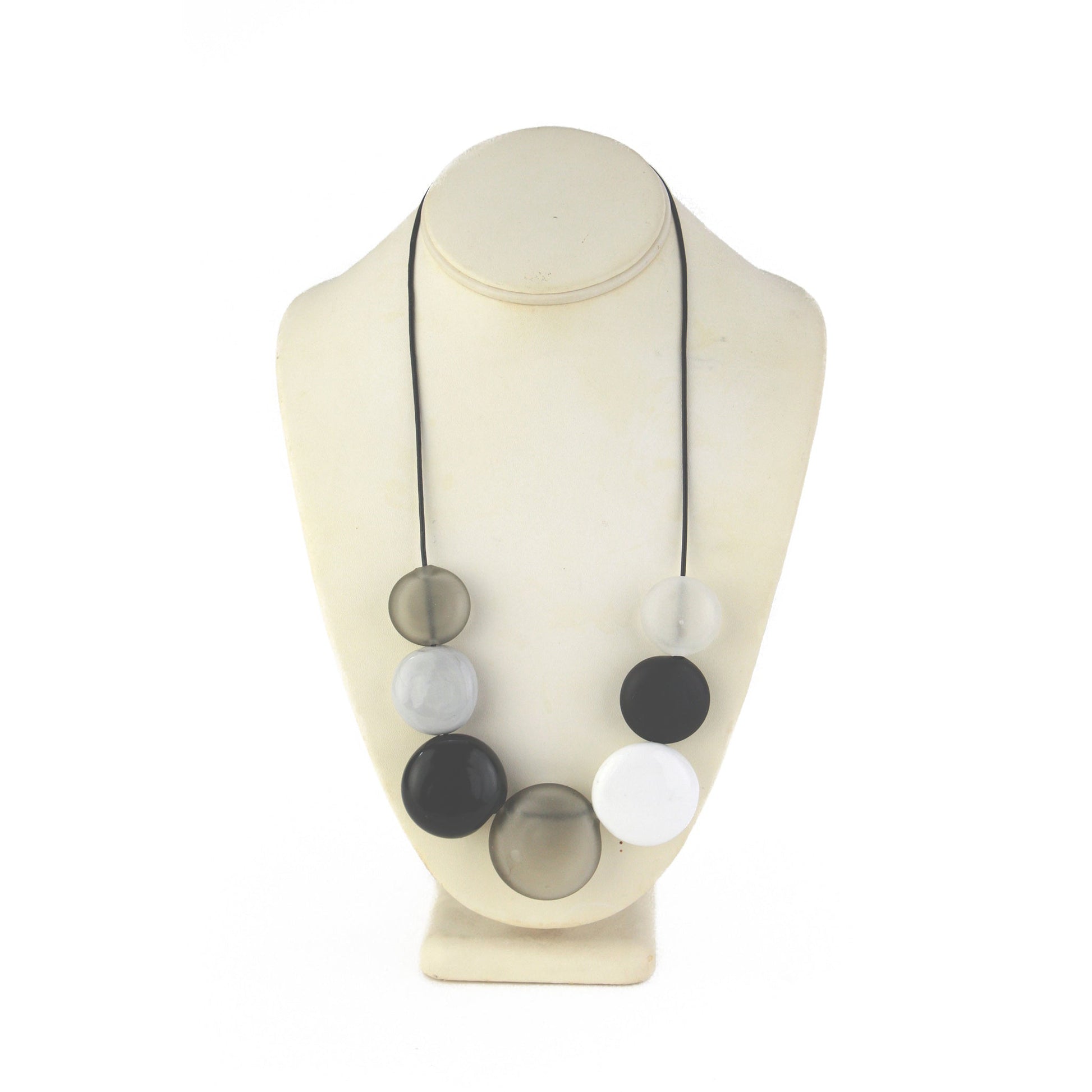 A monochromatic necklace featuring seven hollow, hand-blown glass beads in black, white, grey, and clear tones, strung on adjustable leather for versatile styling.