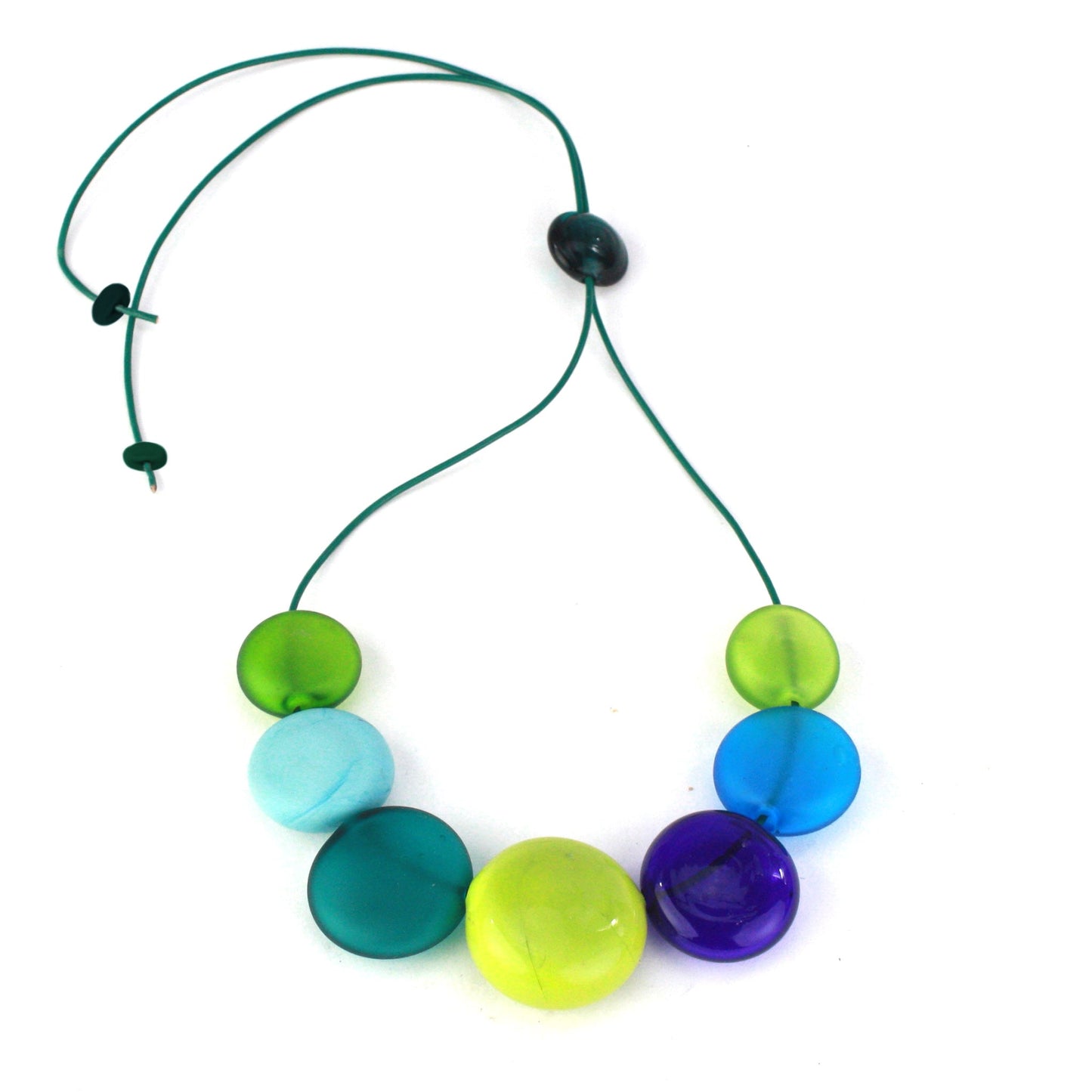 A vibrant necklace featuring seven hollow, hand-blown glass beads in shades of blue, teal, and green, strung on adjustable leather for versatile styling options.
