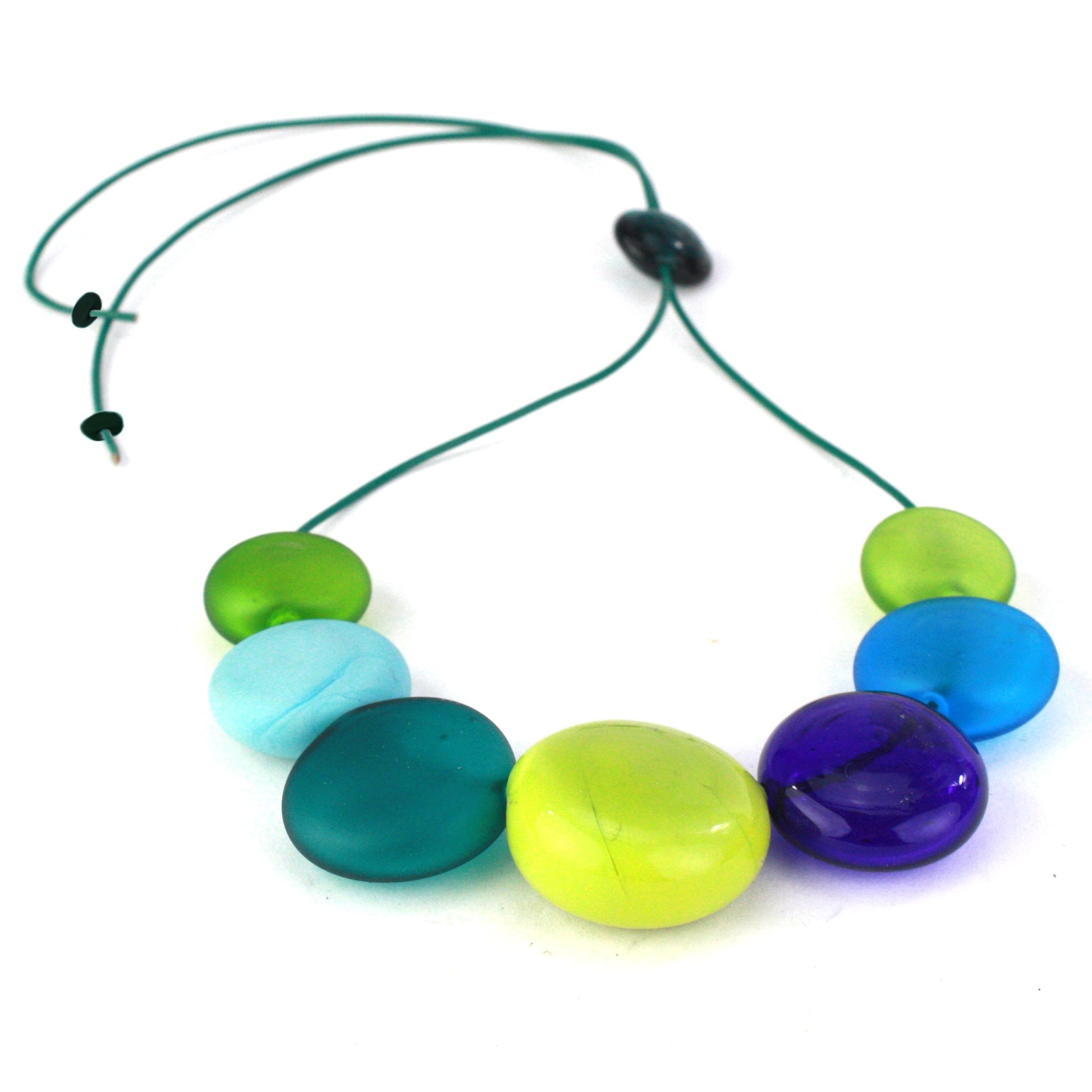 A vibrant necklace featuring seven hollow, hand-blown glass beads in shades of blue, teal, and green, strung on adjustable leather for versatile styling options.