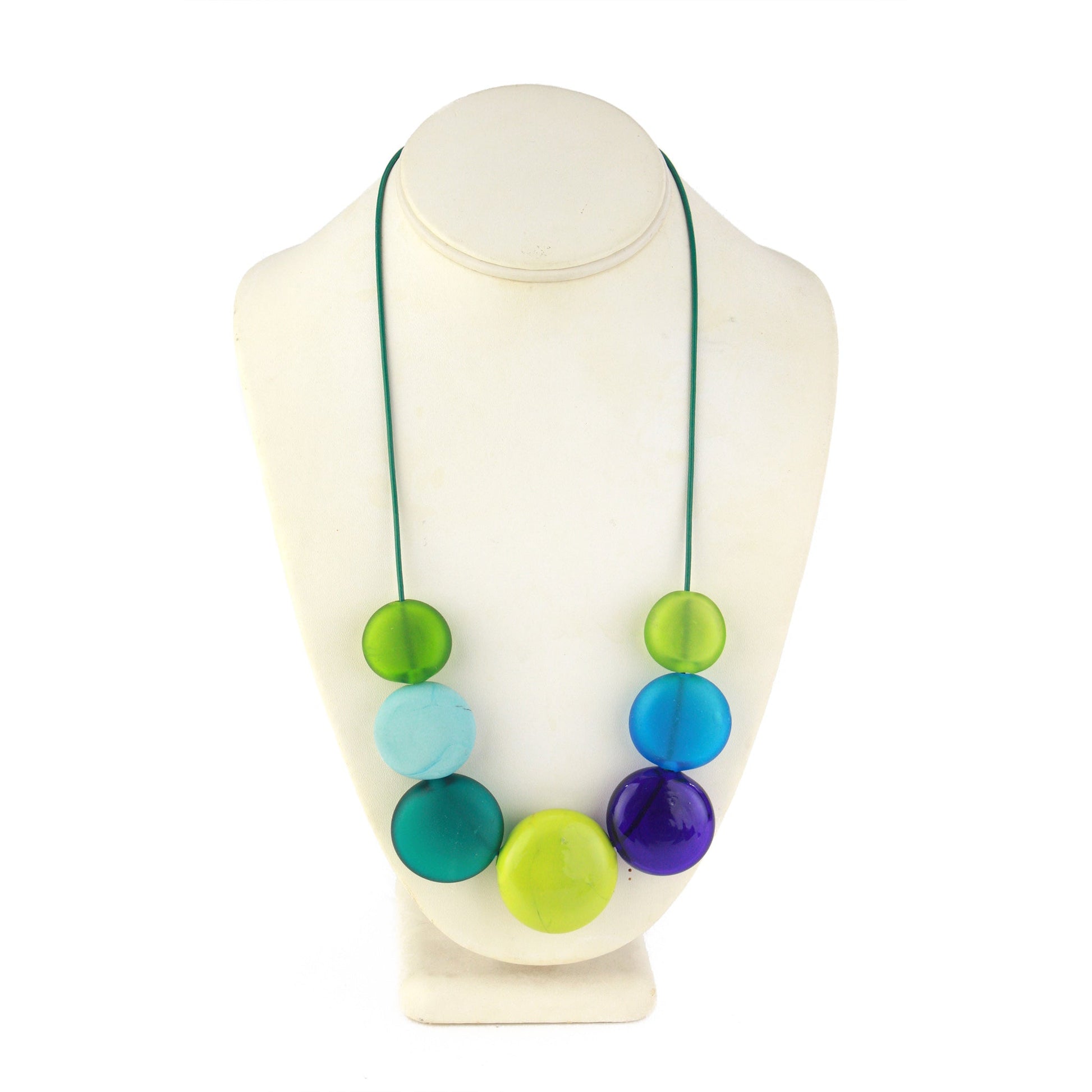 A vibrant necklace featuring seven hollow, hand-blown glass beads in shades of blue, teal, and green, strung on adjustable leather for versatile styling options.