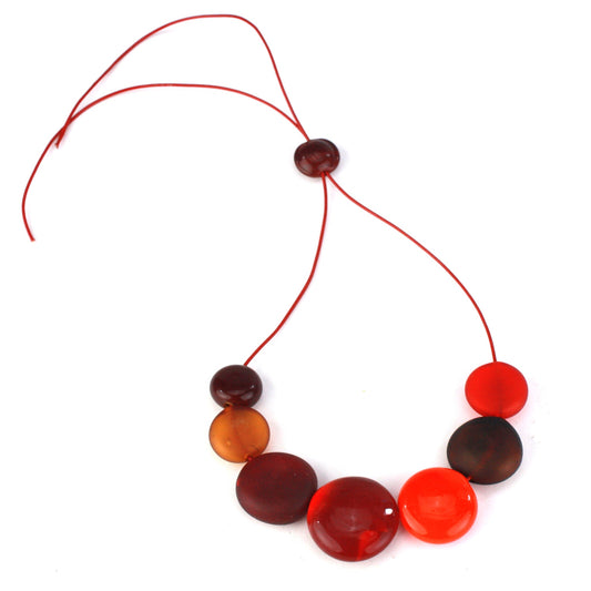 A striking necklace featuring seven hollow, hand-blown glass beads in warm shades of red, orange, and amber, strung on adjustable leather for versatile wear.