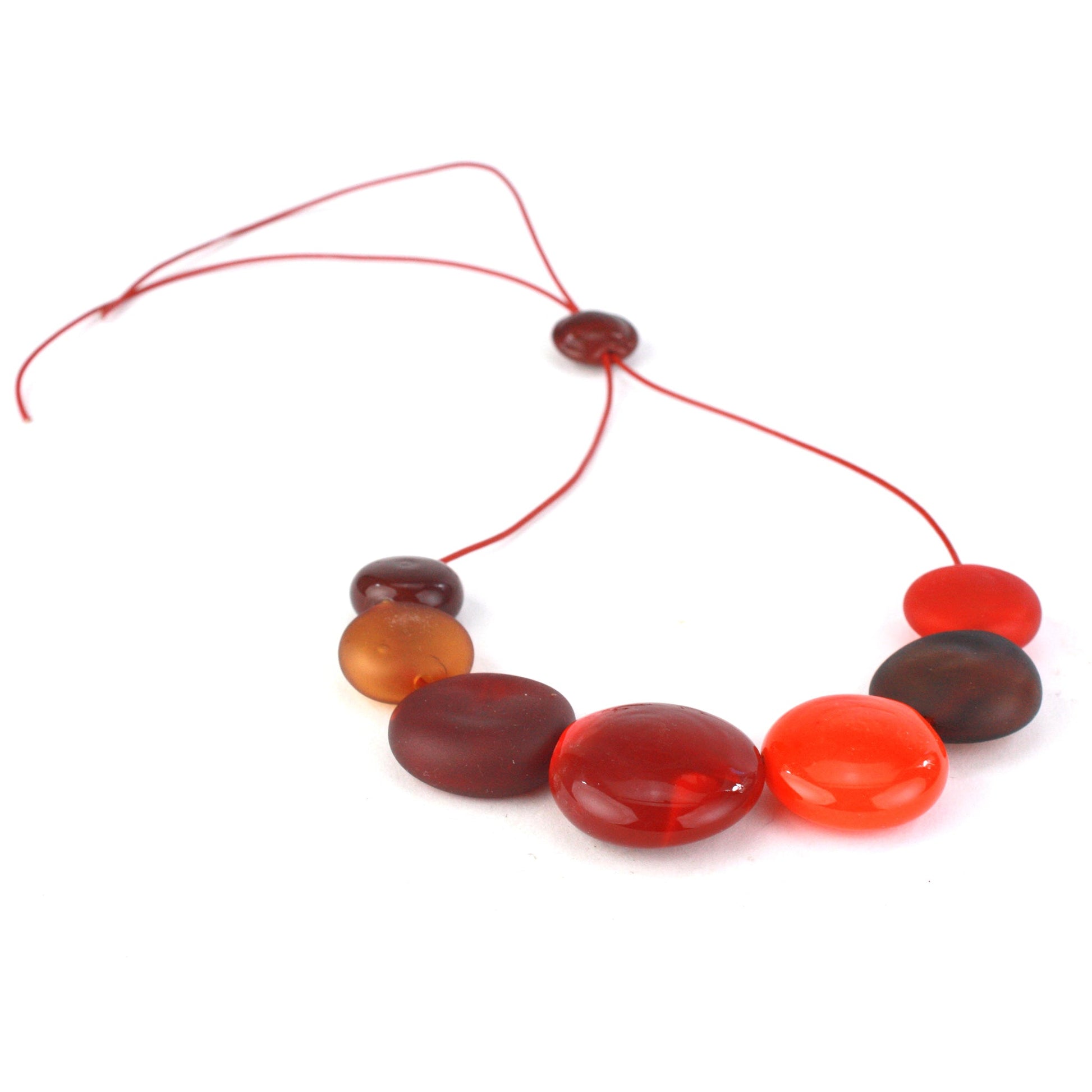 A striking necklace featuring seven hollow, hand-blown glass beads in warm shades of red, orange, and amber, strung on adjustable leather for versatile wear.
