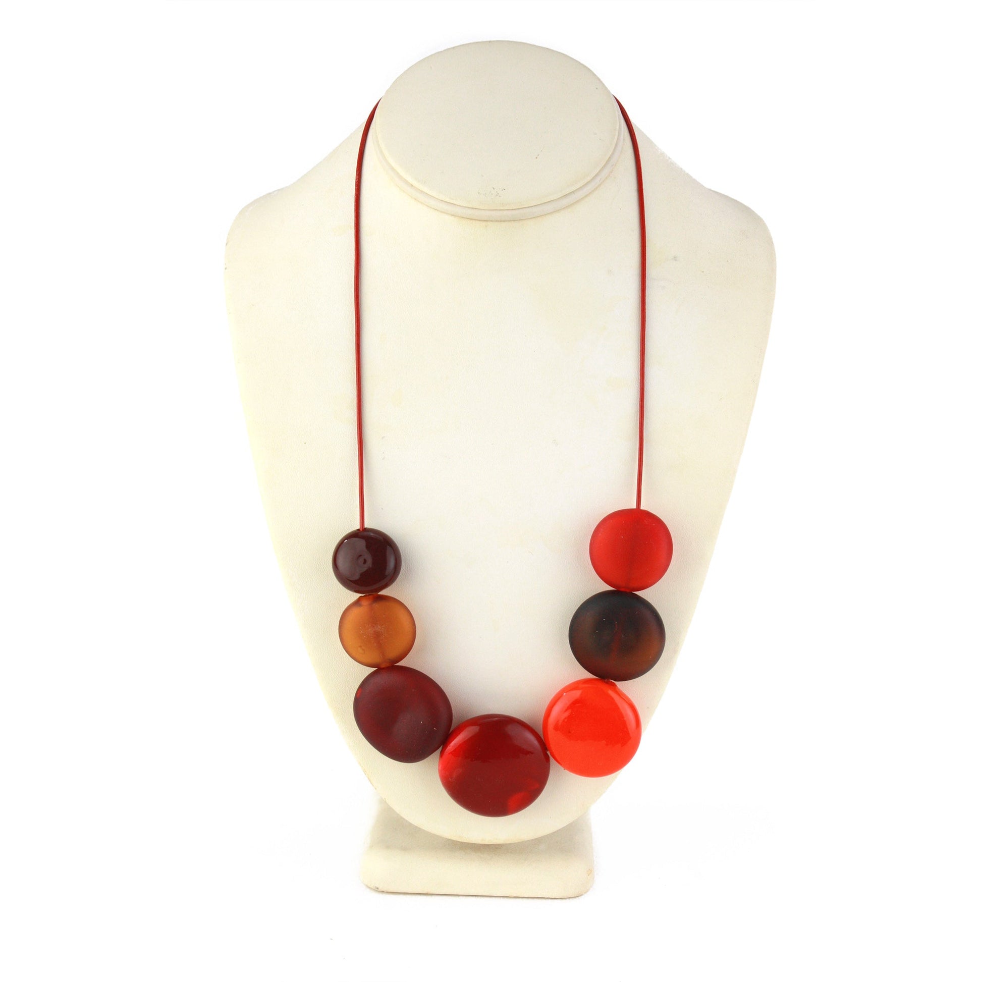 A striking necklace featuring seven hollow, hand-blown glass beads in warm shades of red, orange, and amber, strung on adjustable leather for versatile wear.