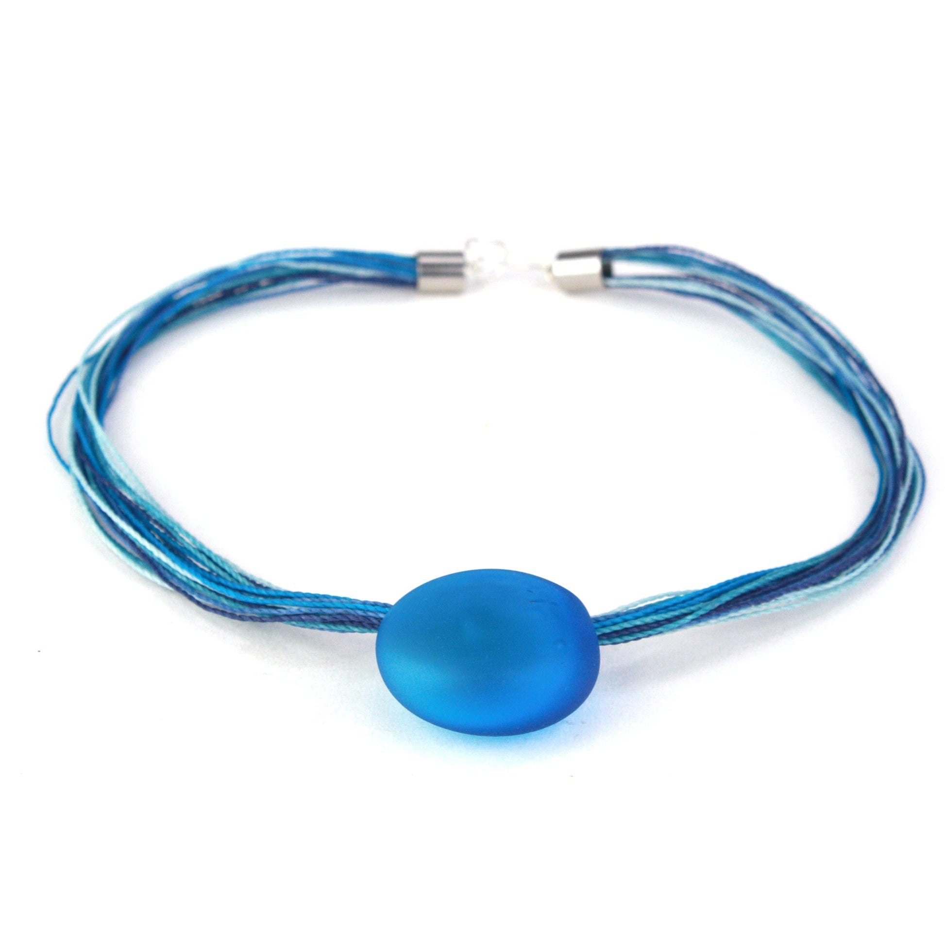A vibrant necklace featuring a hand-blown blue glass focal bead strung on multi-strand waxed cord in coordinating blue tones. Finished with a sterling silver hook-and-loop clasp, this elegant piece adds a bold pop of color to any outfit.