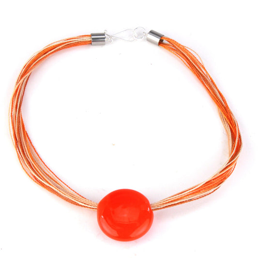 A bold necklace featuring a hand-blown orange glass focal bead strung on multi-strand waxed cord in vibrant shades of orange, cream, and beige. Finished with a sterling silver hook-and-loop clasp, this piece adds a pop of bright color to any outfit.