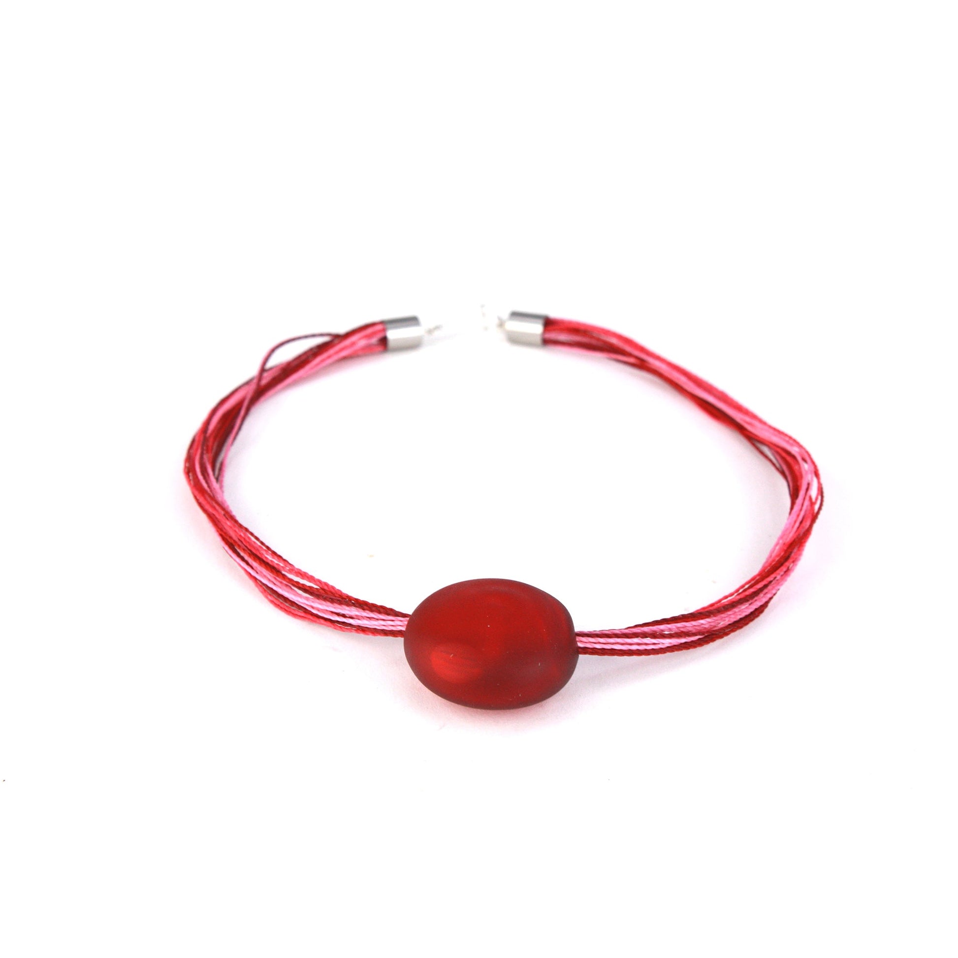 A romantic necklace featuring a hand-blown red glass focal bead strung on multi-strand waxed cord in rich shades of red and pink. Finished with a sterling silver hook-and-loop clasp, this piece adds a bold yet elegant touch to any outfit.