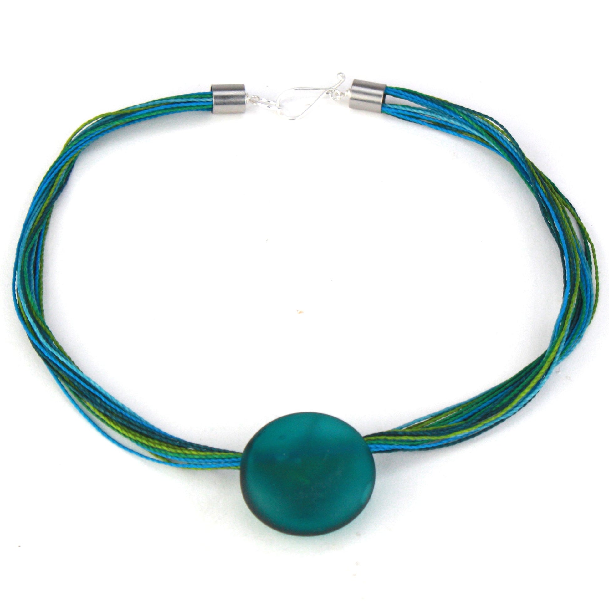 A vibrant necklace featuring a hand-blown teal glass focal bead strung on multi-strand waxed cord in shades of teal and aqua. Finished with a sterling silver hook-and-loop clasp, this piece offers a bold, ocean-inspired accent.