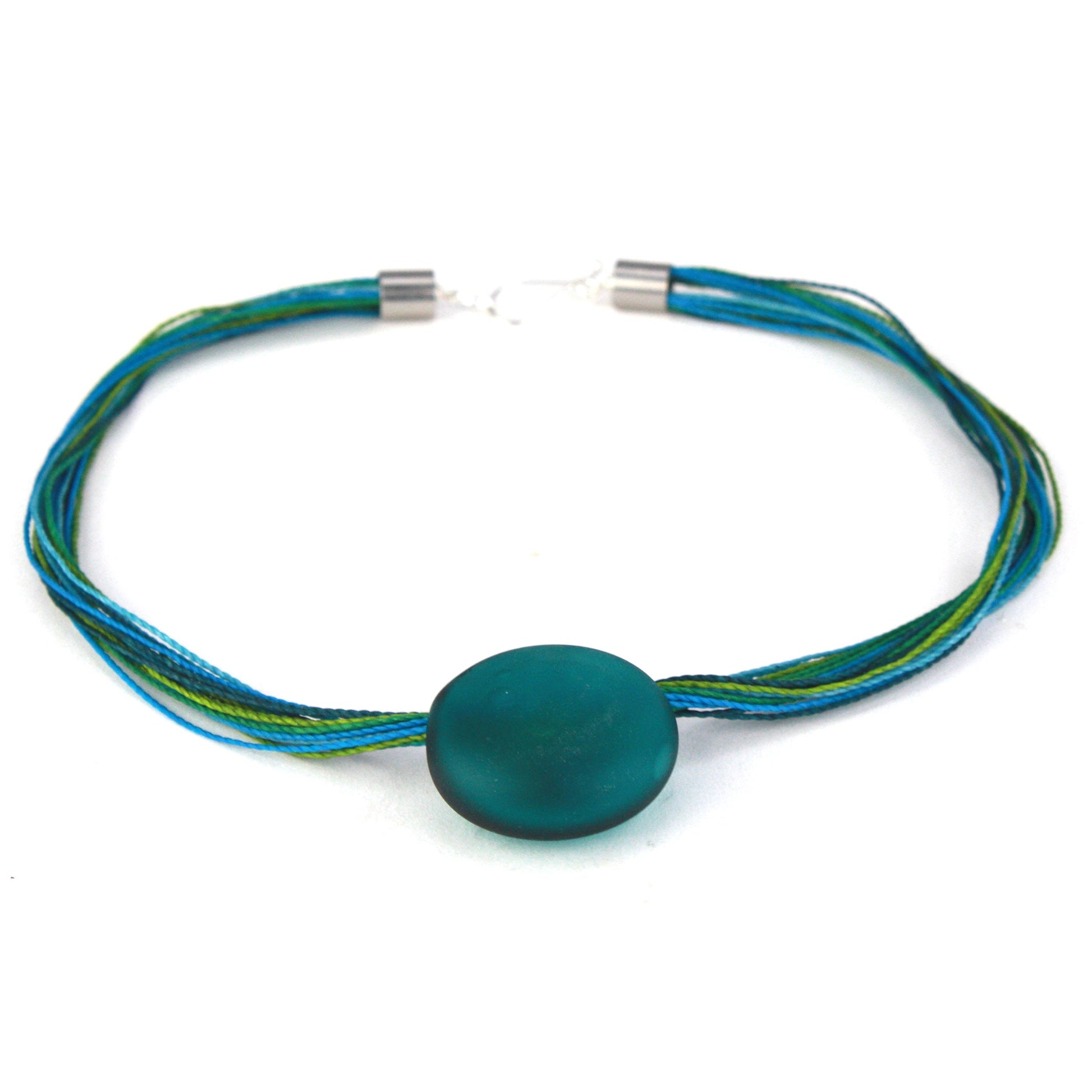 A vibrant necklace featuring a hand-blown teal glass focal bead strung on multi-strand waxed cord in shades of teal and aqua. Finished with a sterling silver hook-and-loop clasp, this piece offers a bold, ocean-inspired accent.