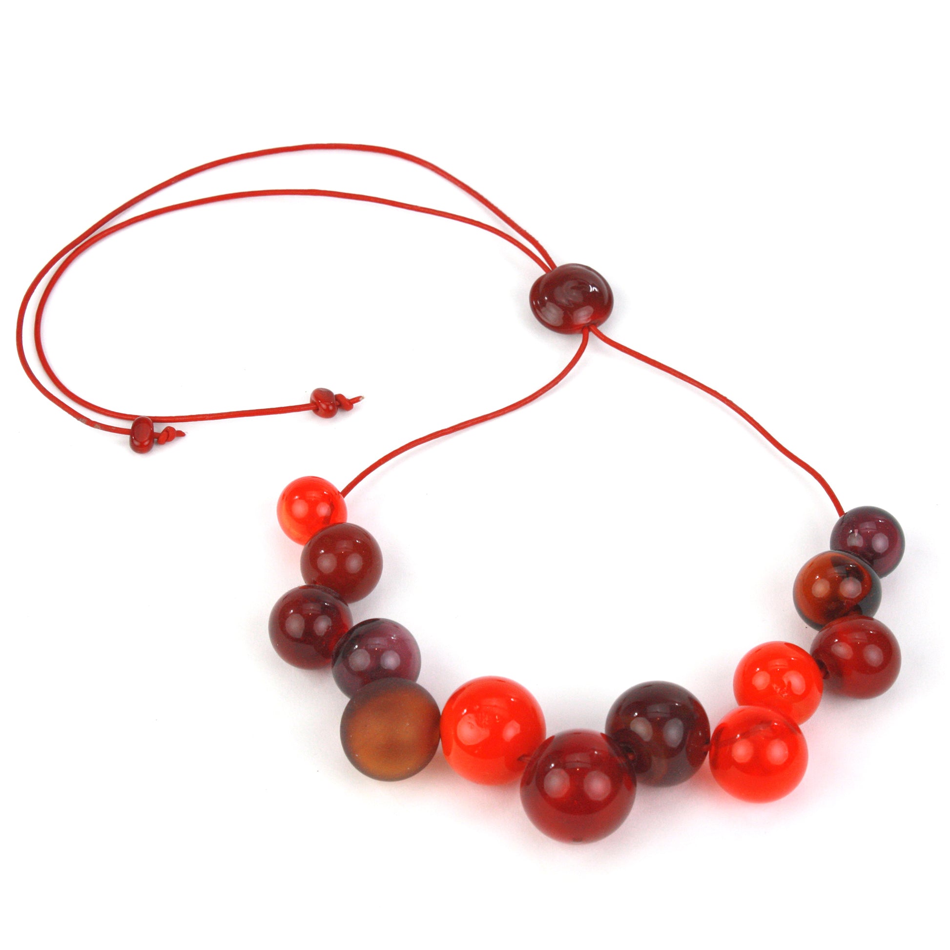 Offset Bolla Necklace featuring hand-blown glass beads in red, amber, and burgundy hues strung on red leather cord with a handcrafted adjustable slider bead.