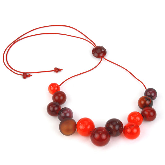 Offset Bolla Necklace featuring hand-blown glass beads in red, amber, and burgundy hues strung on red leather cord with a handcrafted adjustable slider bead.