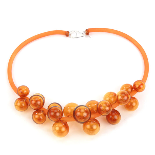 An amber Chroma necklace featuring a cluster of handmade glass beads strung on steel and threaded through a hand-dyed silicone cord with a sterling silver clasp.