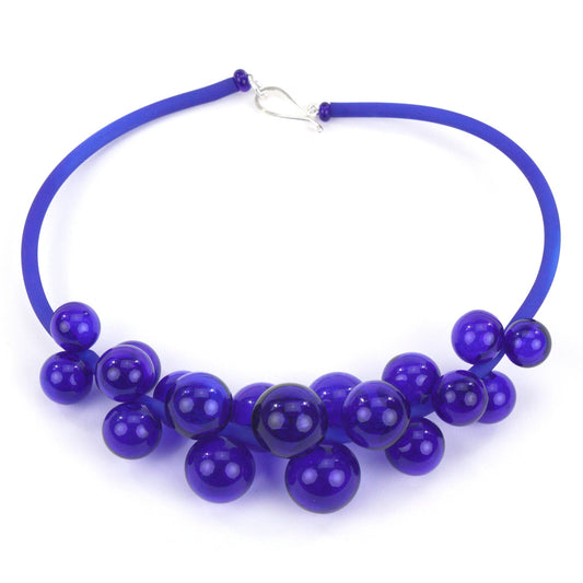 A blue Chroma necklace featuring a cluster of handmade glass beads strung on steel and threaded through a hand-dyed silicone cord with a sterling silver clasp.