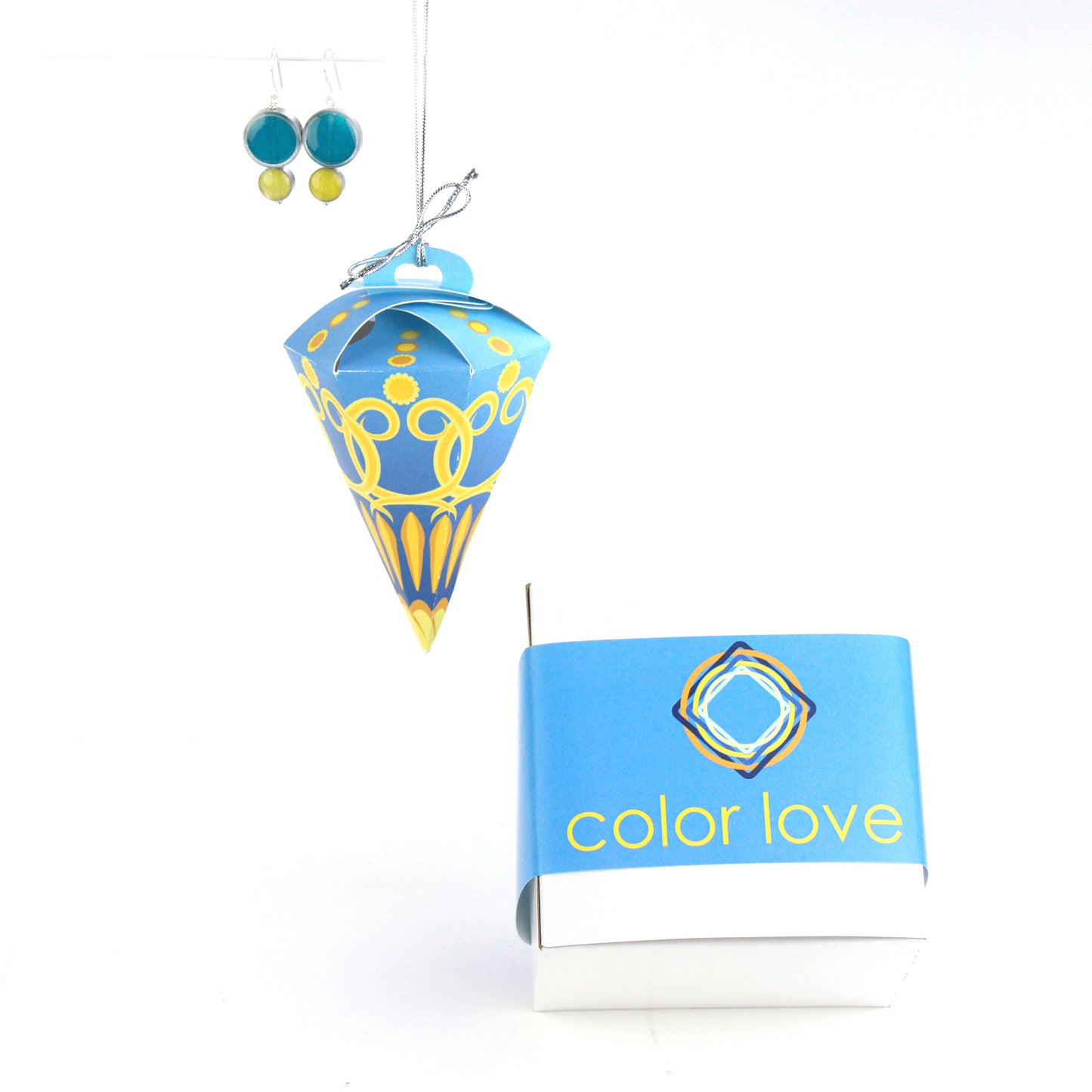 A pair of double-circle earrings in turquoise and yellow displayed alongside a blue and yellow festive ornament box, designed for hanging, and a coordinating Color Love-branded gift box.