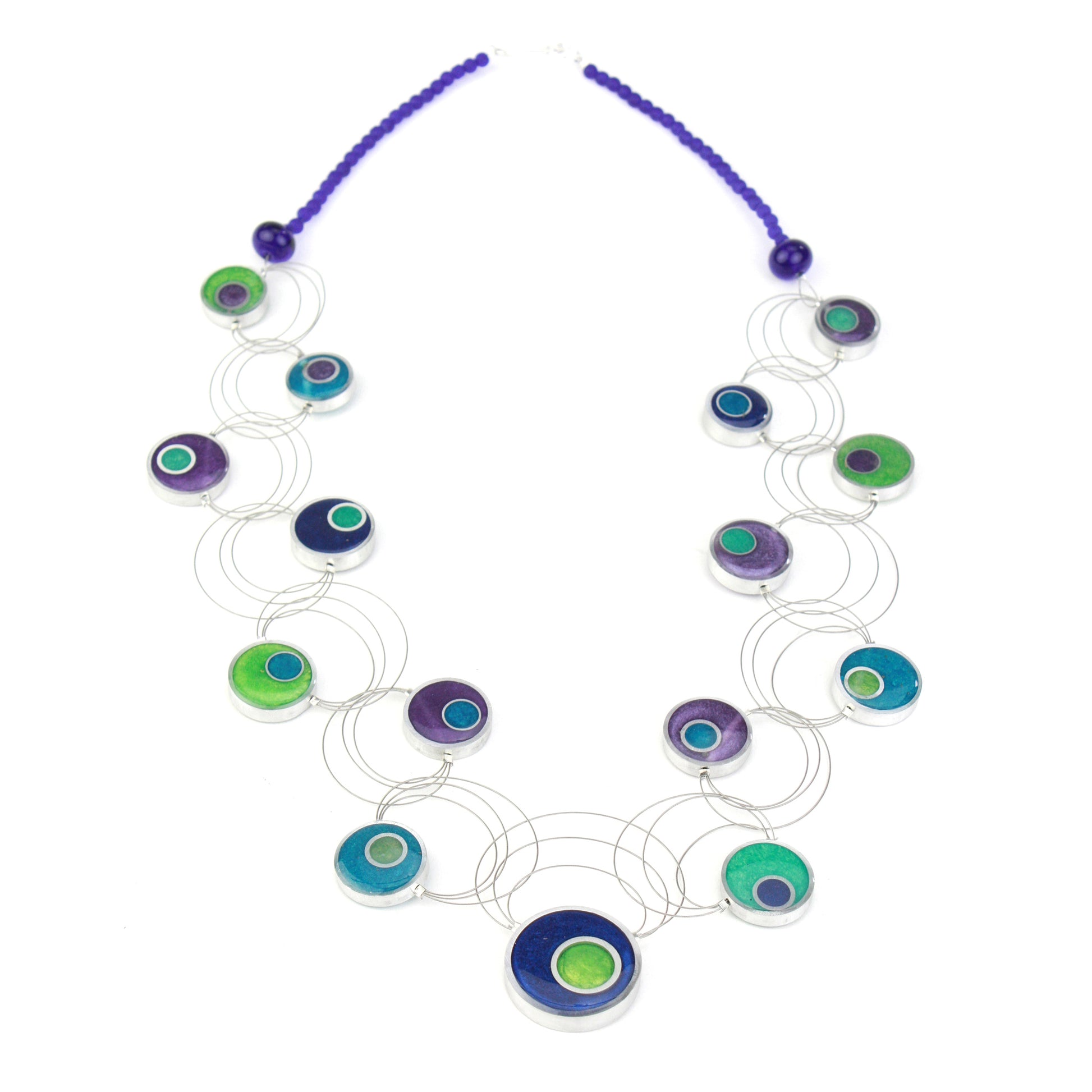 A handcrafted necklace featuring intertwining steel cables adorned with circular eco-resin and salvaged aluminum beads in shades of blue, green, and purple.