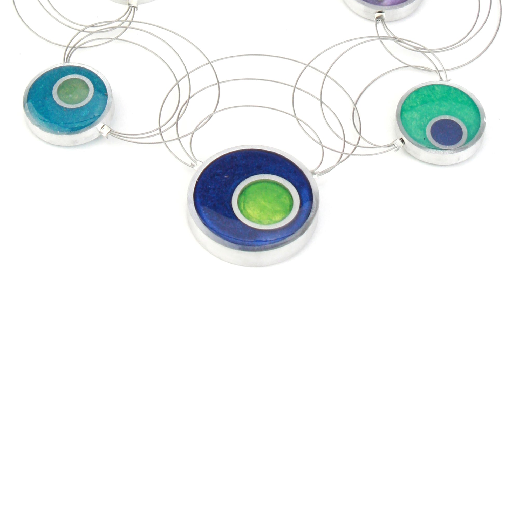 A handcrafted necklace featuring intertwining steel cables adorned with circular eco-resin and salvaged aluminum beads in shades of blue, green, and purple.