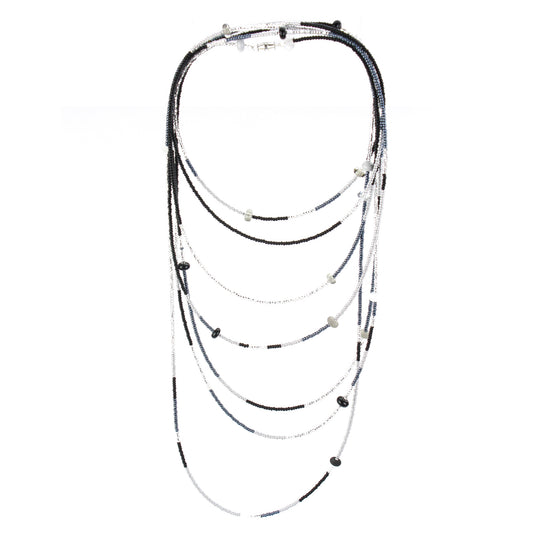 A long, multi-strand necklace featuring a mix of black, white, and silver glass seed beads, accented with handcrafted lampworked glass beads. The necklace is secured with a barrel screw clasp and offers a versatile, elegant design perfect for layering or wearing long.