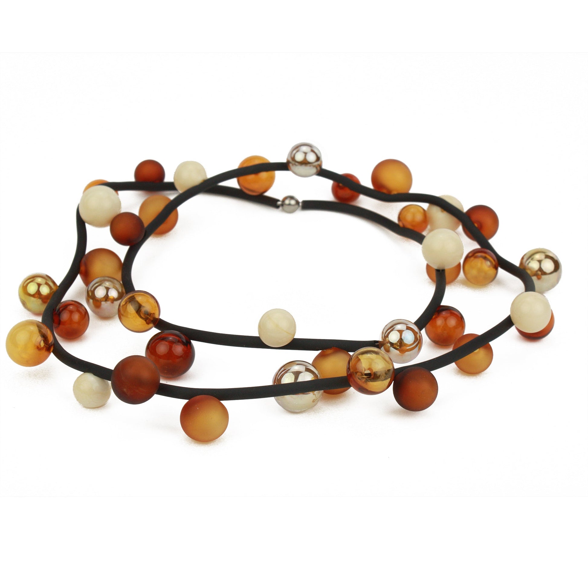 The "Bolla" necklace featuring hand-blown glass beads in amber, gold, and cream tones, strung on a steel cable through a rubber cord, worn long or doubled up.