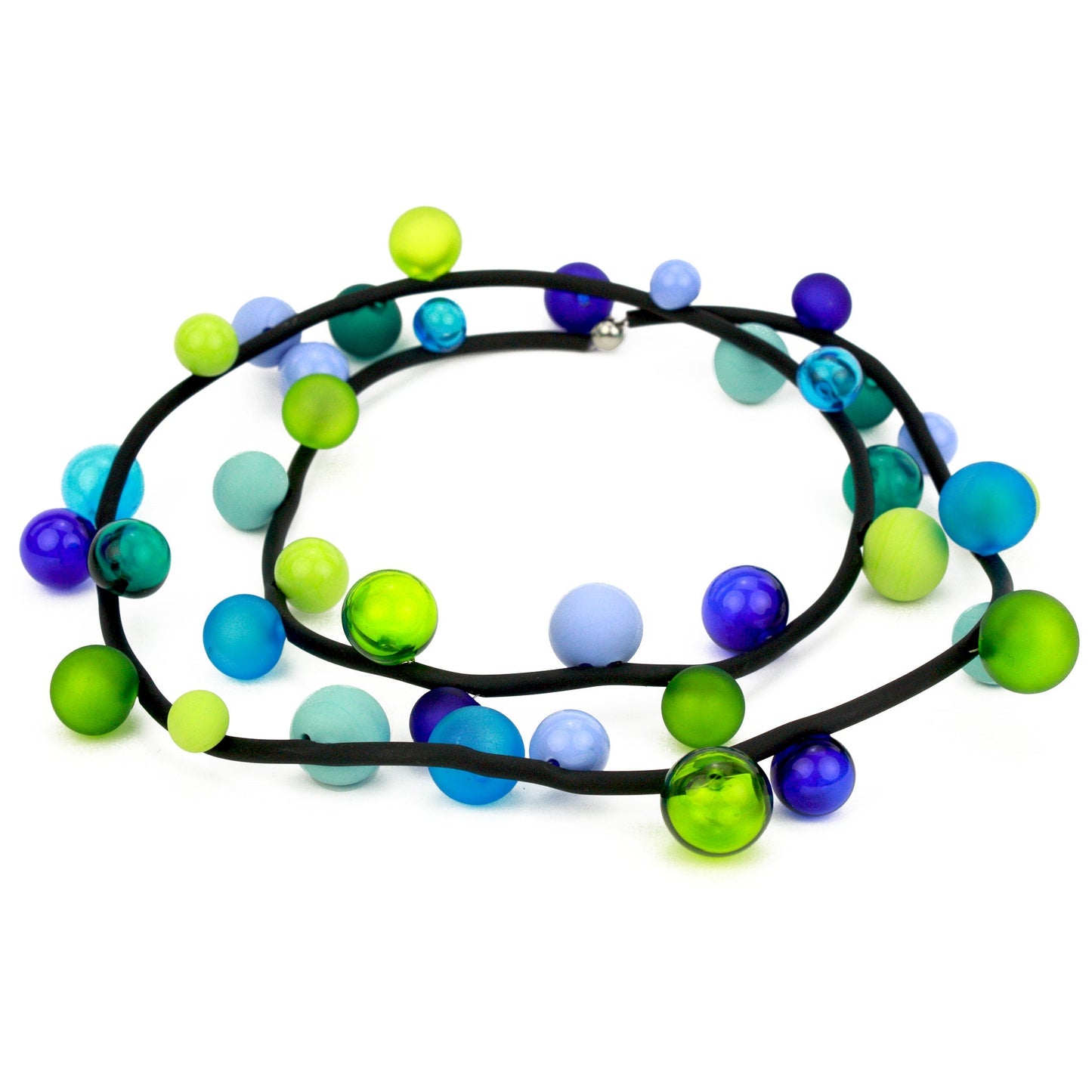 The "Bolla" necklace featuring hand-blown glass beads in shades of blue, green, and teal, strung on a steel cable threaded through a rubber cord, worn long or doubled.