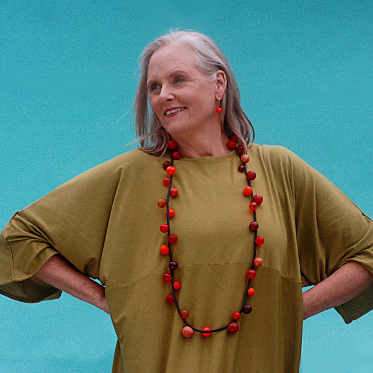 "Bolla" necklace with hand-blown glass beads in red, orange, and amber tones, strung on a steel cable within a rubber cord, shown in a long style.