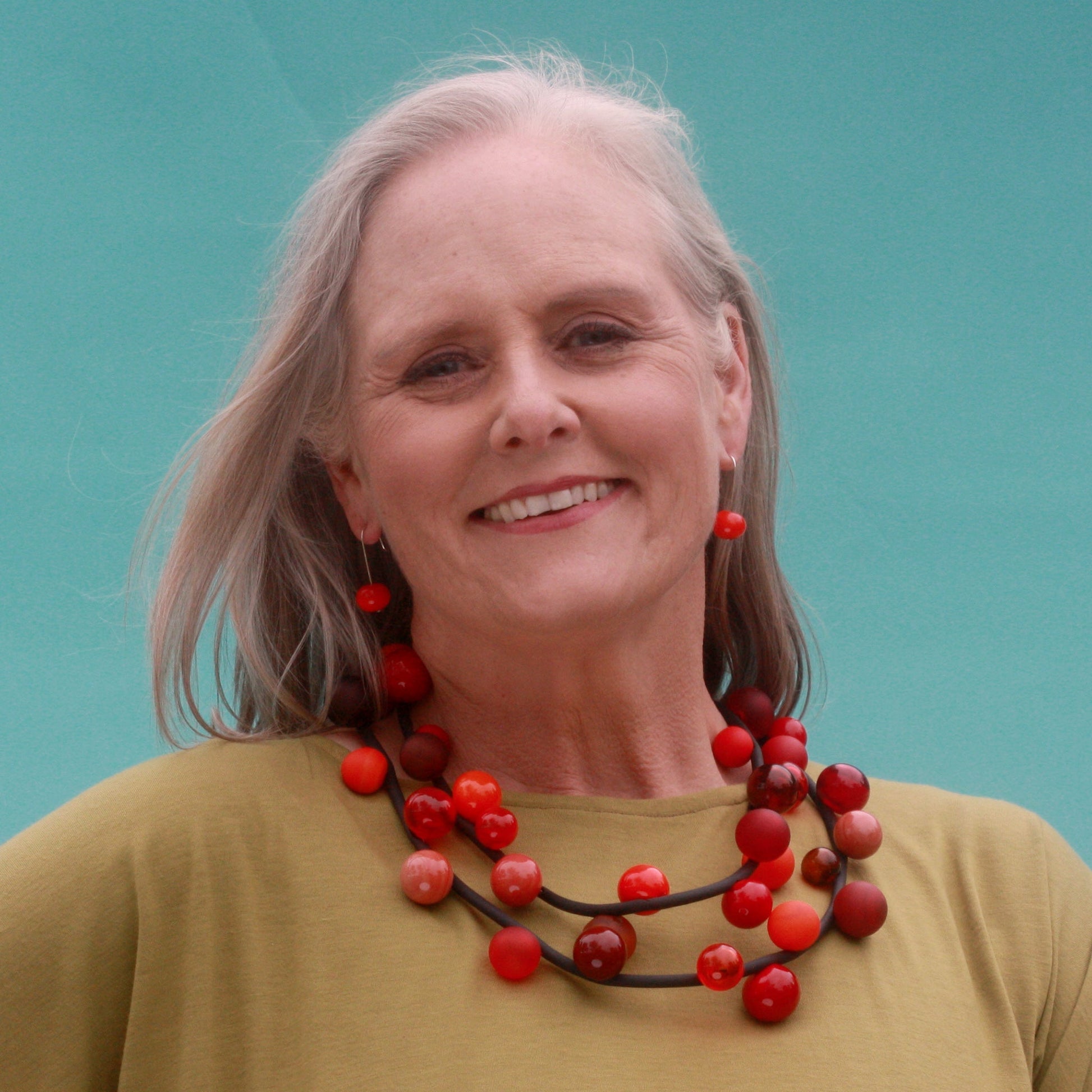 "Bolla" necklace with hand-blown glass beads in red, orange, and amber tones, strung on a steel cable within a rubber cord, shown in a long style.