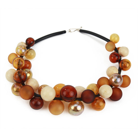 A bold statement necklace featuring hand-blown glass beads in warm shades of amber, gold, cream, and bronze, strung on steel cable through a rubber cord with a sterling silver clasp.