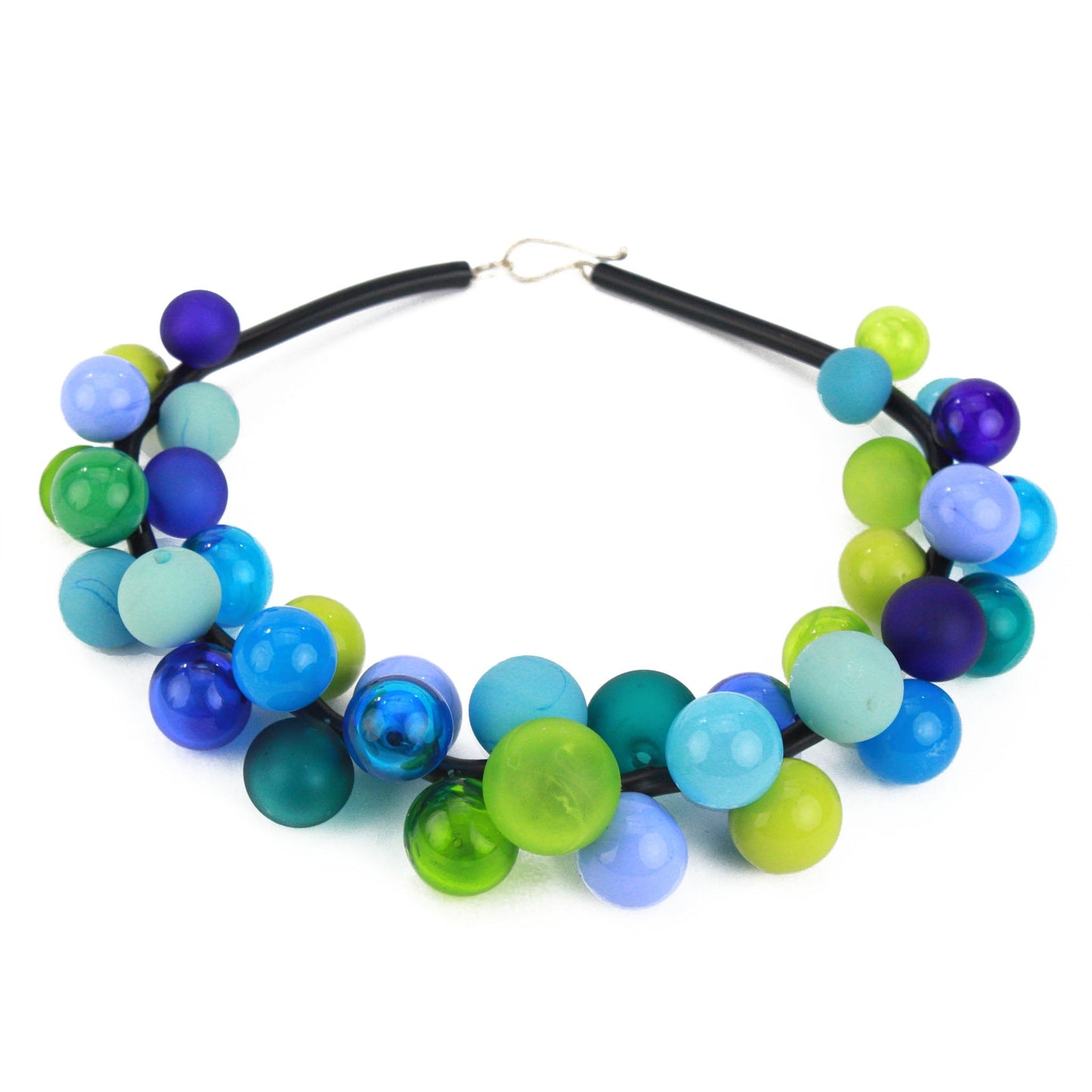 The "Bolla" necklace featuring hand-blown glass beads in shades of blue, green, and teal, strung on a steel cable threaded through a rubber cord with a sterling silver clasp.