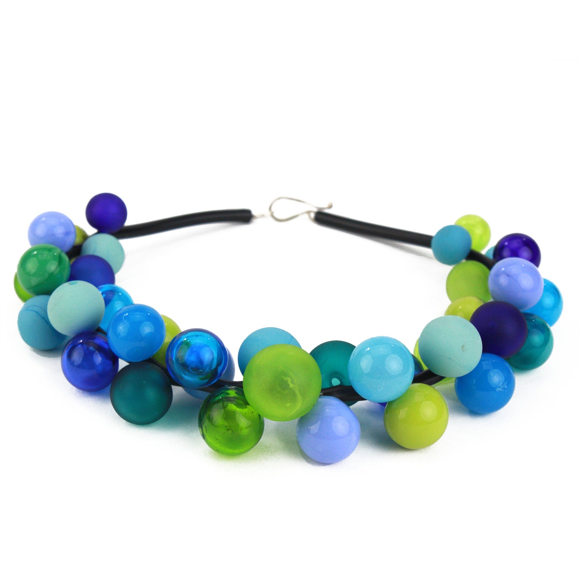 The "Bolla" necklace featuring hand-blown glass beads in shades of blue, green, and teal, strung on a steel cable threaded through a rubber cord with a sterling silver clasp.