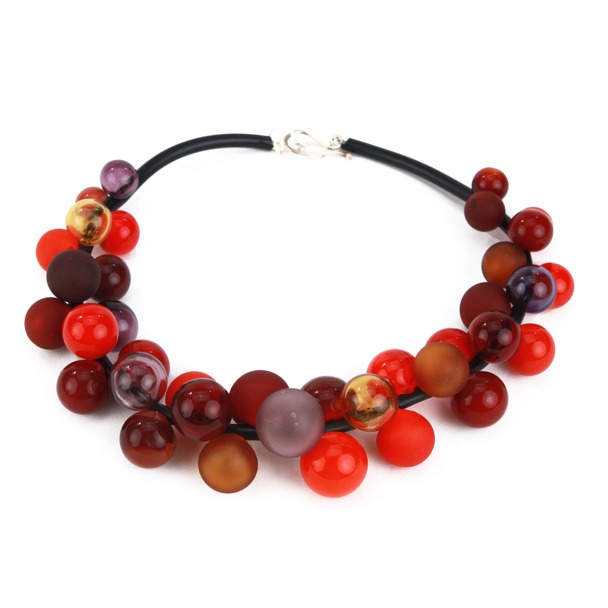 The "Bolla" necklace featuring hand-blown glass beads in shades of red, maroon, and amber, strung on a steel cable threaded through a rubber cord with a sterling silver clasp.