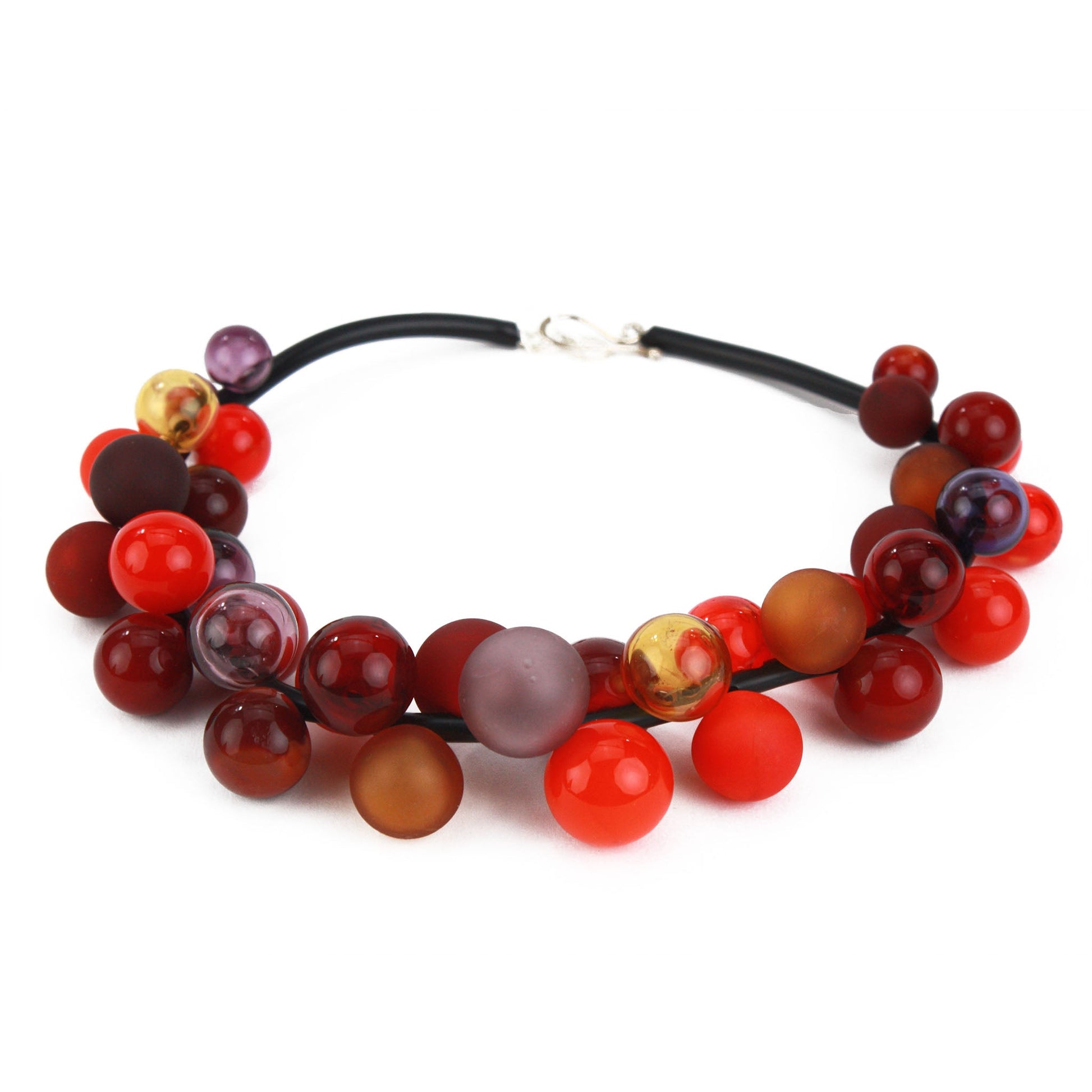 The "Bolla" necklace featuring hand-blown glass beads in shades of red, maroon and amber, strung on a steel cable threaded through a rubber cord with a sterling silver clasp.