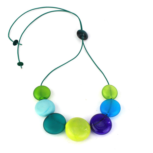 A vibrant necklace featuring seven hollow, hand-blown glass beads in shades of blue, teal, and green, strung on adjustable leather for versatile styling options.

