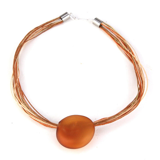 A necklace featuring a hand-blown amber glass focal bead strung on colorful multi-strand waxed cord. Finished with a sterling silver hook-and-loop clasp, this elegant piece combines warm tones with artisanal craftsmanship.