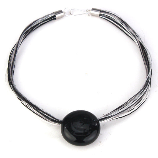 A sleek necklace featuring a hand-blown black glass focal bead strung on multi-strand waxed cord in black and silver tones. Finished with a sterling silver hook-and-loop clasp, this elegant piece offers a modern and sophisticated look.