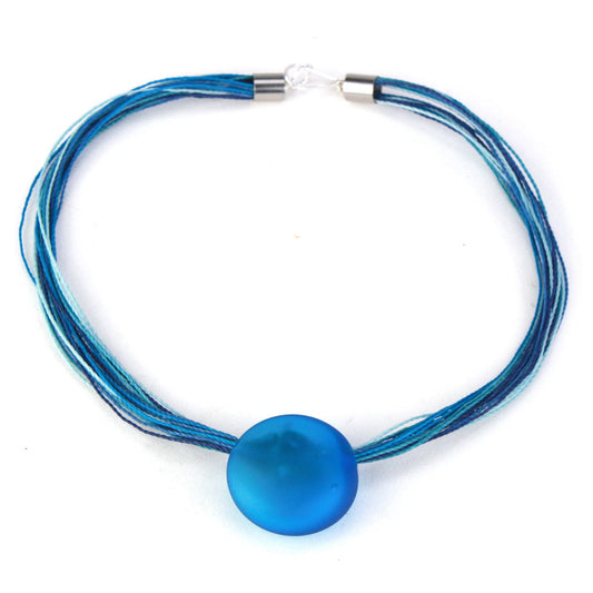 A vibrant necklace featuring a hand-blown blue glass focal bead strung on multi-strand waxed cord in coordinating blue tones. Finished with a sterling silver hook-and-loop clasp, this elegant piece adds a bold pop of color to any outfit.