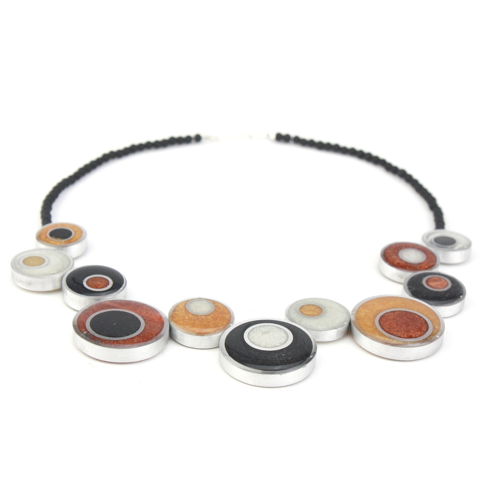 A handcrafted offset necklace featuring eco-resin and salvaged aluminum beads in black, white, copper, and gold tones, accented with glass beads and a silver clasp.