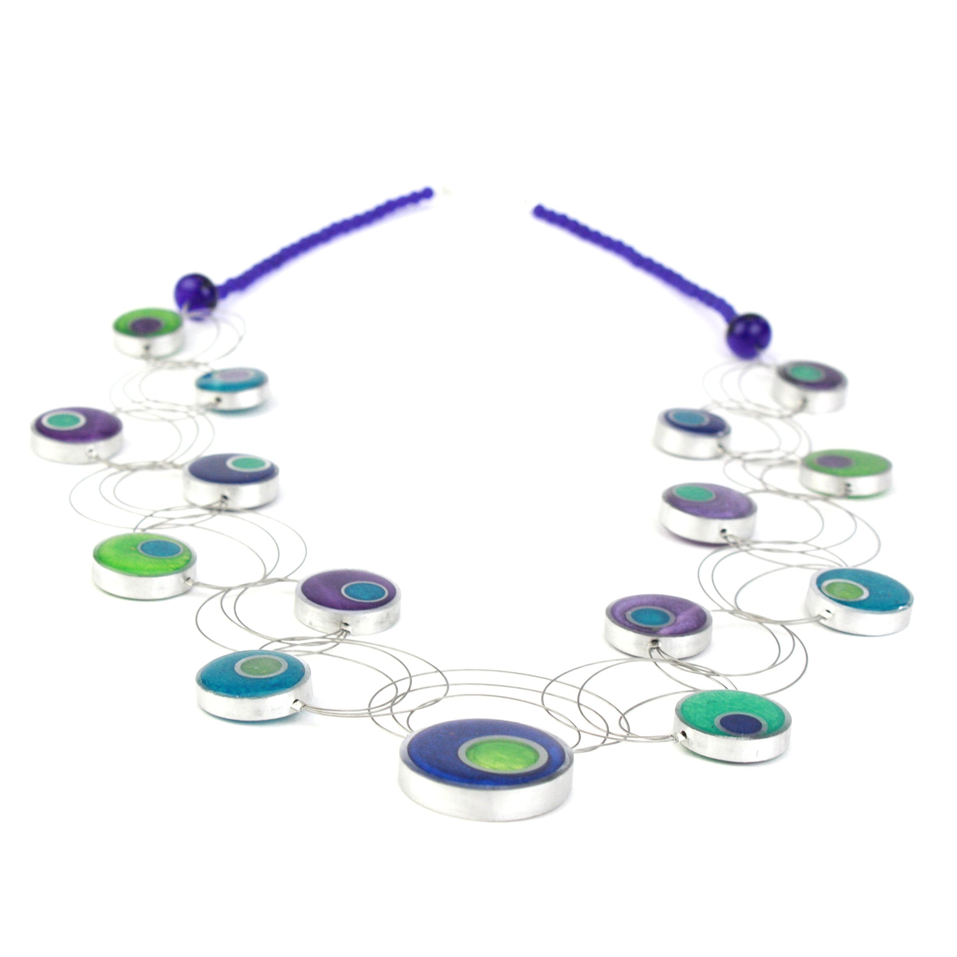 A handcrafted necklace featuring intertwining steel cables adorned with circular eco-resin and salvaged aluminum beads in shades of blue, green, and purple.