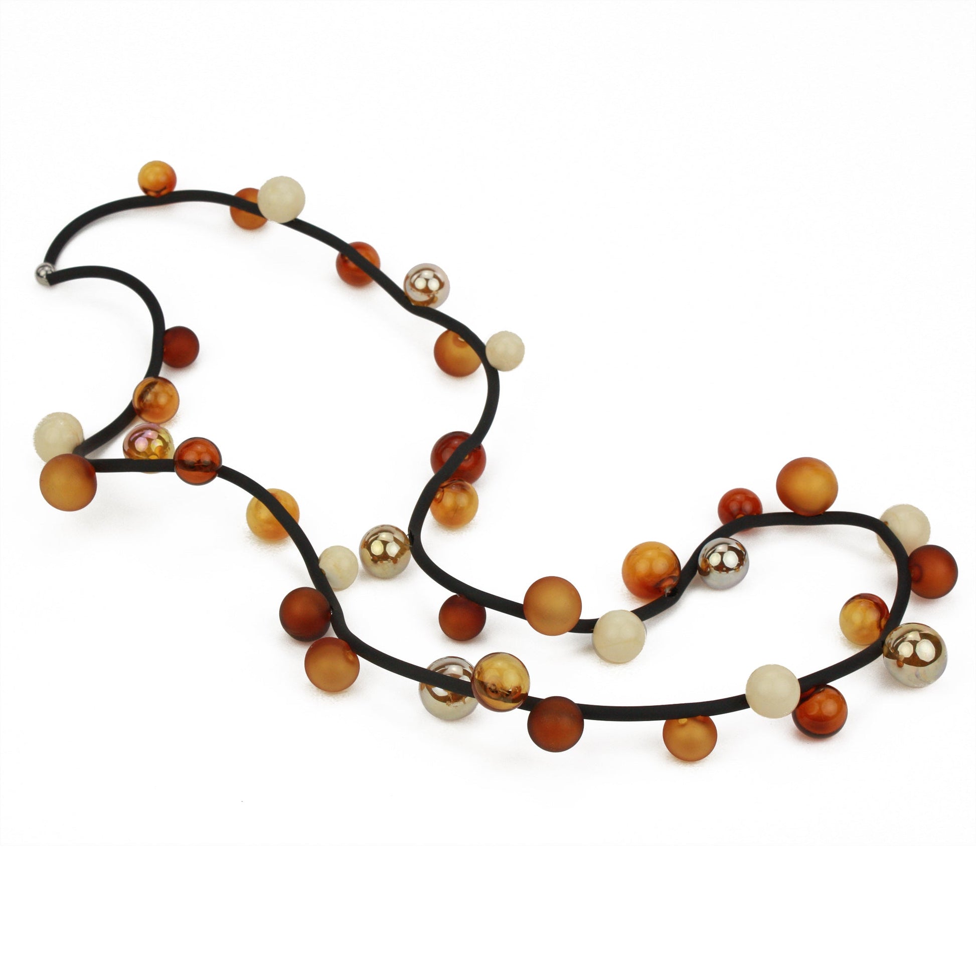 The "Bolla" necklace featuring hand-blown glass beads in amber, gold, and cream tones, strung on a steel cable through a rubber cord, worn long or doubled up.