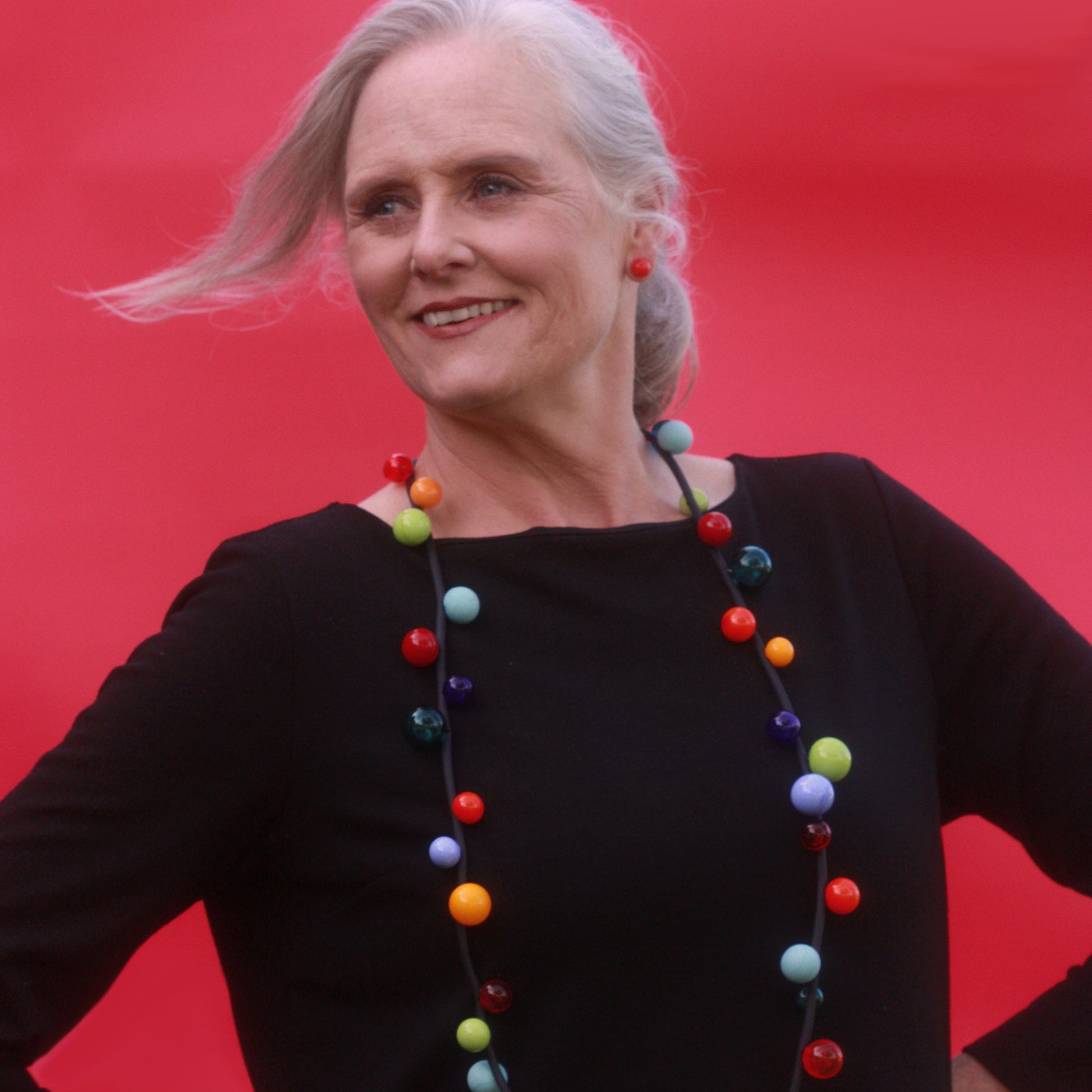 "Bolla" necklace featuring vibrant hand-blown glass beads in rainbow colors, strung on a steel cable threaded through a rubber cord, worn long or doubled.

