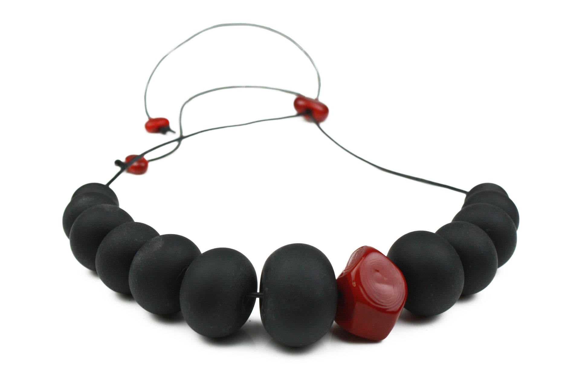 Necklace of hand blown and sandblasted hollow beads in velvety black glass paired with a red glass nugget bead and strung on adjustable leather