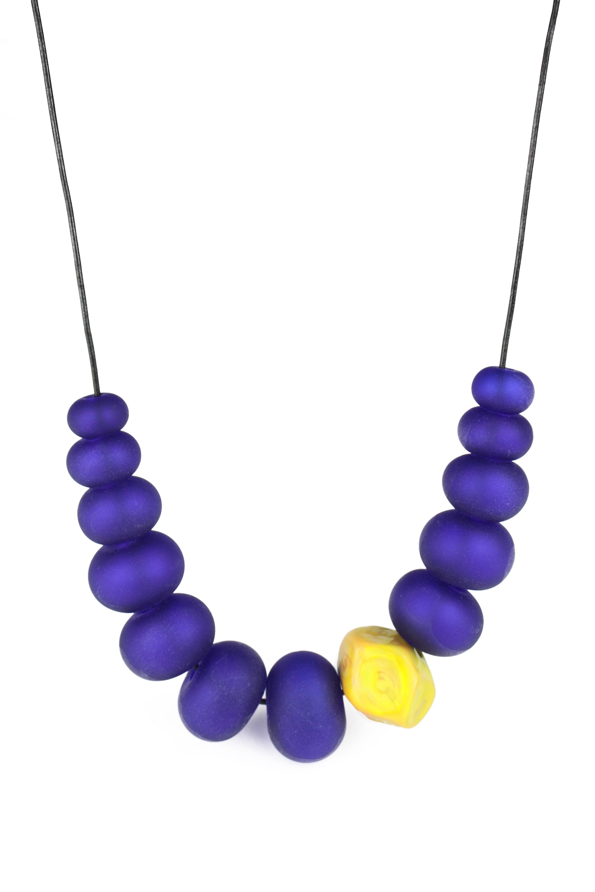 Necklace of hand blown and sandblasted hollow beads in cobalt blue glass paired with a ochre yellow glass nugget bead and strung on adjustable leather