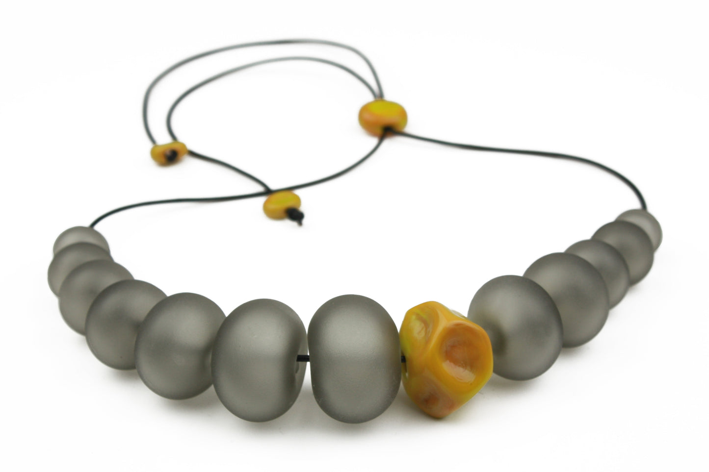 Necklace of hand blown and sandblasted hollow beads in velvety grey glass paired with a ochre yellow glass nugget bead and strung on adjustable leather